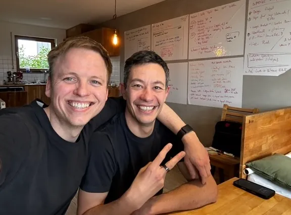 Paul Miedl and Fabian Zentel laughing into the camera, with whiteboards full of RankingRakete.ai notes behind them